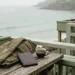 Leere Hotelterrasse am Meer im Morgenlicht, auf dem Tisch eine gefaltete Jacke und ein geschlossener Reisepass