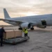 Bestatter bringen eine neutrale Holztransportkiste auf einem Rollwagen zum Frachtraum eines Flugzeugs