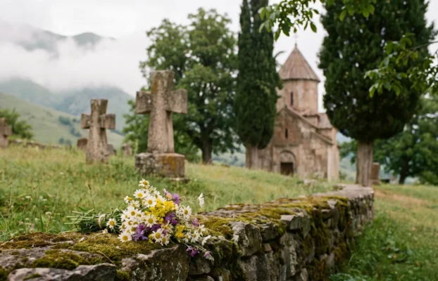 Friedhof mit Steinkreuzen und kleiner Kirche vor Berglandschaft im Kaukasus im Morgenlicht