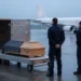 Sarg auf einem Rollwagen am Luftfrachtterminal, im Hintergrund ein Passagierflugzeug