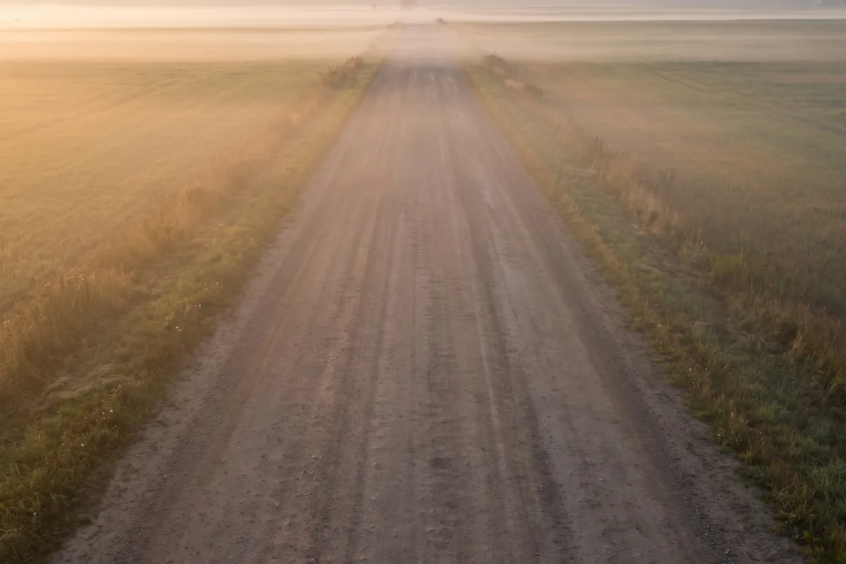Leere Landstraße durch weite Felder in Osteuropa im Morgennebel bei Sonnenaufgang
