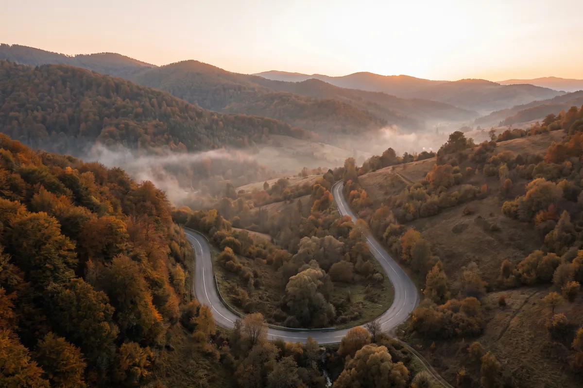 Kurvige leere Bergstraße durch herbstliche Wälder der Karpaten mit Nebel in den Tälern