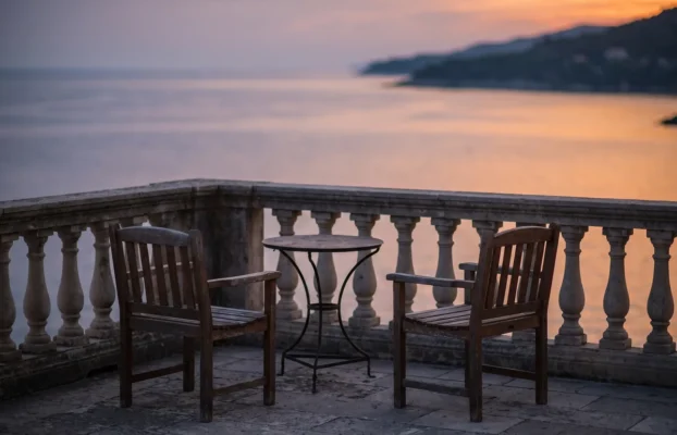 Leere Hotelterrasse mit zwei Stühlen und kleinem Tisch mit Blick auf das ruhige Meer im Abendlicht