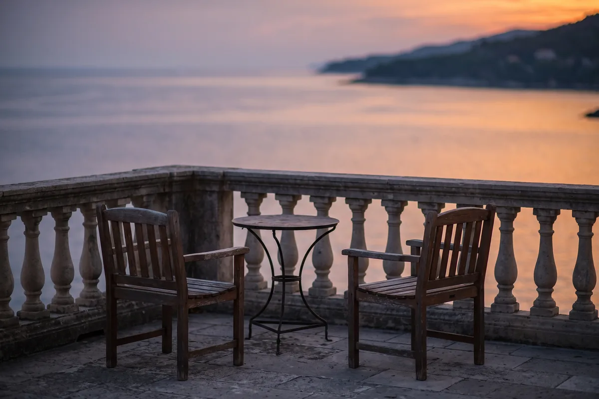 Leere Hotelterrasse mit zwei Stühlen und kleinem Tisch mit Blick auf das ruhige Meer im Abendlicht